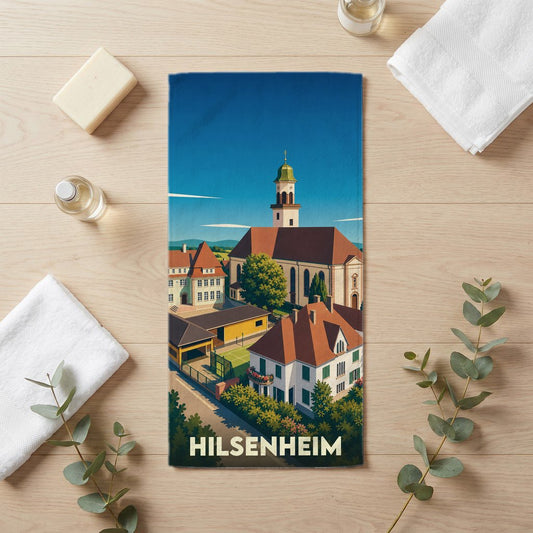 Serviette de bain souvenir de la ville de Hilsenheim avec une illustration graphique colorée de son église et de ses bâtiments.