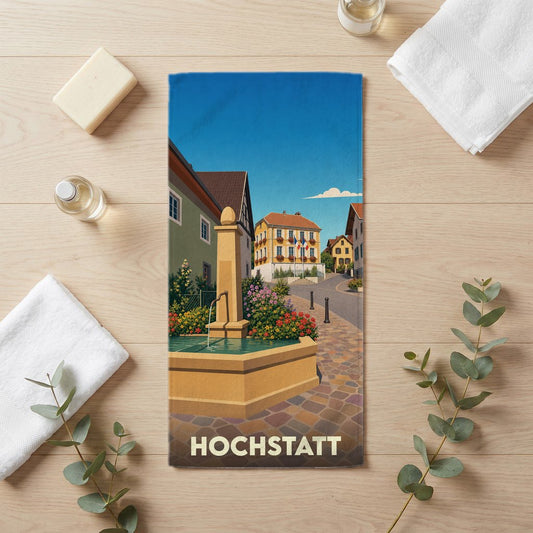 Serviette de bain souvenir de la ville de Hochstatt avec une illustration stylisée d'une fontaine et de maisons traditionnelles.