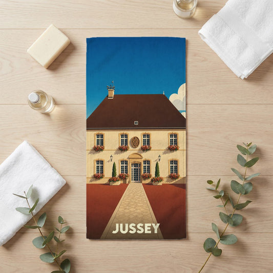 Serviette de bain souvenir de la ville de Jussey avec une illustration stylisée d'un bâtiment historique.