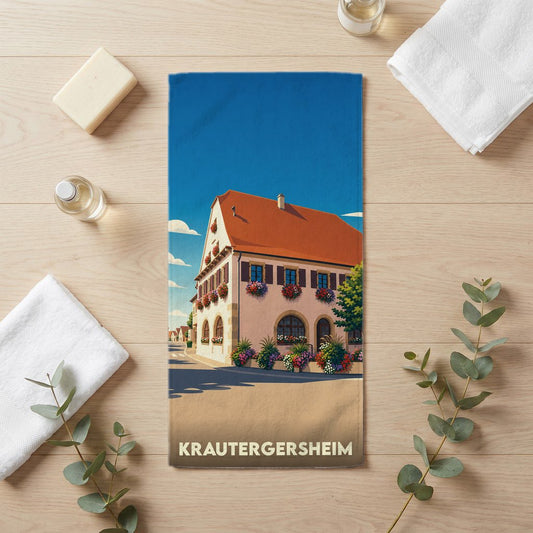 Serviette de bain souvenir de Krautergersheim illustrée d'une maison alsacienne fleurie sous un ciel bleu.