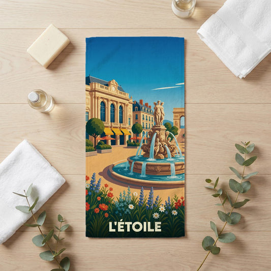 Serviette de bain souvenir de la ville de L'Étoile avec une illustration stylisée d'une fontaine et de bâtiments classiques.