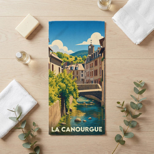 Serviette de bain souvenir de la ville de La Canourgue avec une illustration stylisée d'un canal et de maisons anciennes.