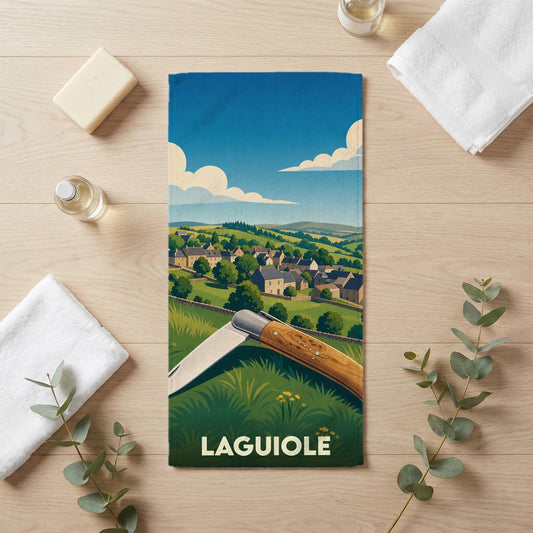 Serviette de bain souvenir de la ville de Laguiole avec une illustration stylisée d'un couteau devant un paysage de campagne.