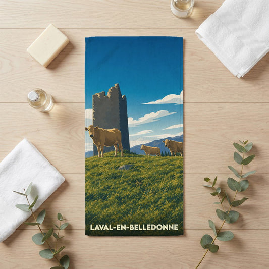 Serviette de bain souvenir de Laval-en-Belledonne illustrée d'un paysage pastoral avec une tour médiévale et des vaches.