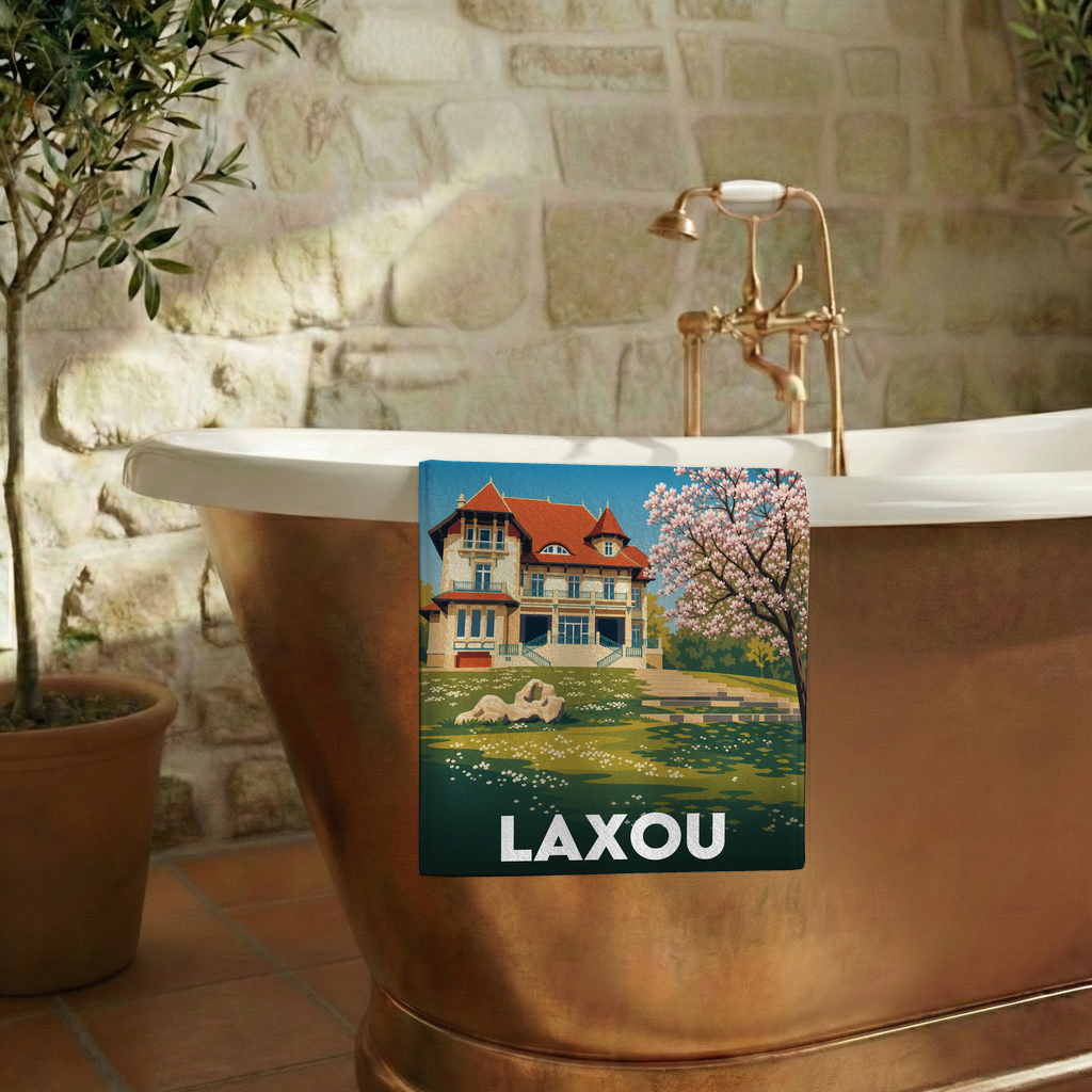 Serviette de bain souvenir de la ville de Laxou avec une illustration stylisée d'une villa et d'un arbre en fleurs.