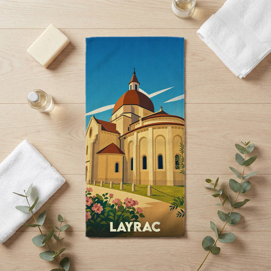Serviette de bain souvenir de la ville de Layrac illustrée d'une église de style roman sous un ciel bleu.