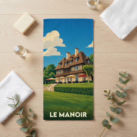 Serviette de bain souvenir de la ville de Le Manoir avec une illustration stylisée d'un manoir normand.