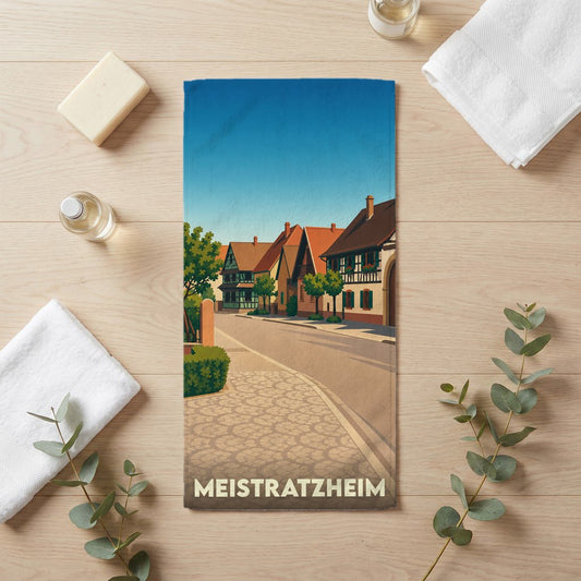 Serviette de bain souvenir de la ville de Meistratzheim illustrée d'un paysage urbain traditionnel alsacien.