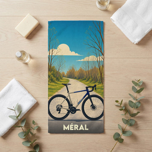 Serviette de bain souvenir de la ville de Méral illustrée d'un vélo sur une route de campagne.