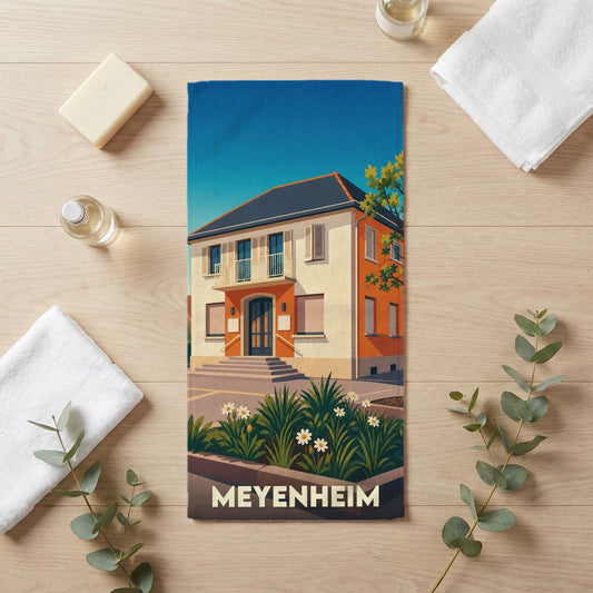Serviette de bain souvenir de la ville de Meyenheim avec une illustration stylisée d'une maison traditionnelle.