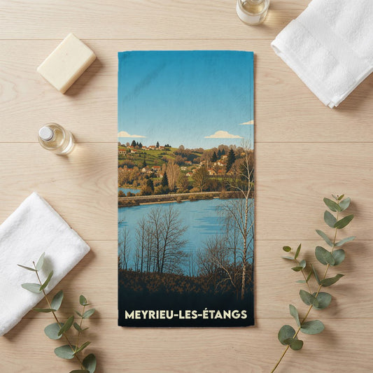 Serviette de bain souvenir de Meyrieu-les-Étangs avec une illustration stylisée d'un paysage de lac et de collines.