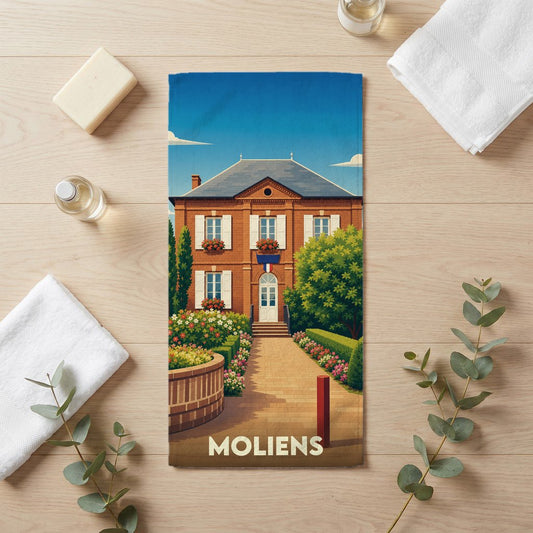 Serviette de bain souvenir de la ville de Moliens illustrée d'une bâtisse traditionnelle en briques sous un ciel bleu.