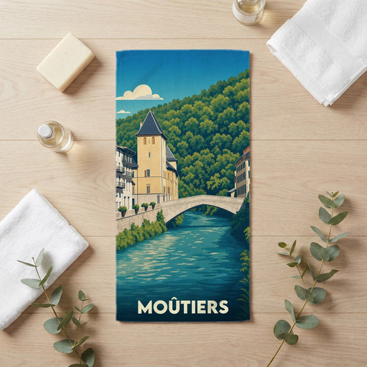 Serviette de bain souvenir de la ville de Moûtiers avec une illustration stylisée d'un pont et d'une tour médiévale.