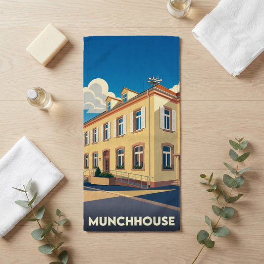 Serviette de bain souvenir de la ville de Munchhouse illustrée d'un bâtiment stylisé sous un ciel bleu.