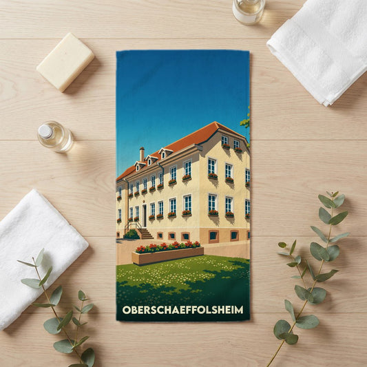 Serviette de bain souvenir de la ville d'Oberschaeffolsheim avec une illustration stylisée d'un bâtiment traditionnel.
