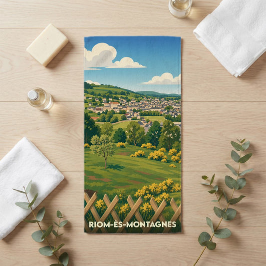 Serviette de bain souvenir de la ville de Riom-ès-Montagnes avec une illustration stylisée de son paysage vallonné.