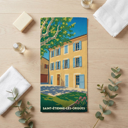 Serviette de bain souvenir de Saint-Étienne-les-Orgues avec une illustration stylisée d'une maison provençale.