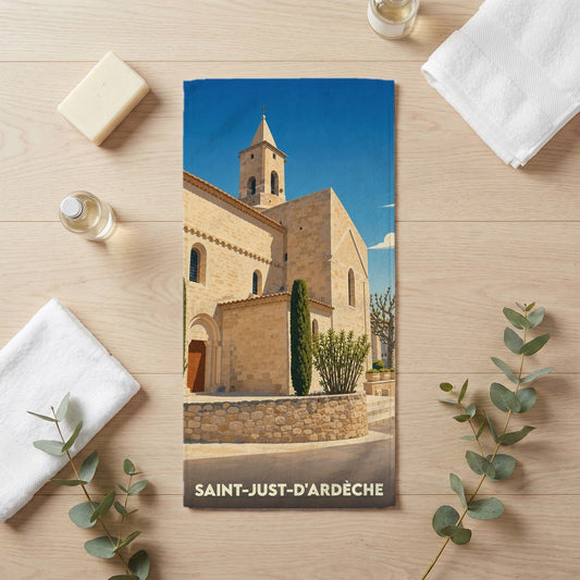 Serviette de bain souvenir de la ville de Saint-Just-d'Ardèche illustrant son église en pierre sous un ciel bleu.