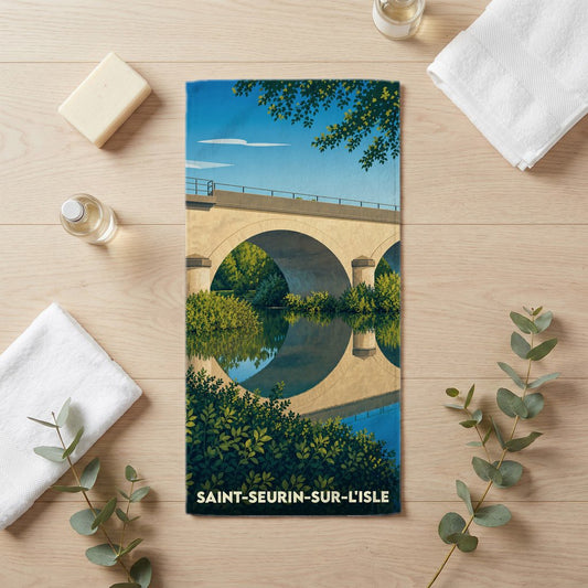 Serviette de bain souvenir de Saint-Seurin-sur-l'Isle illustrée d'un pont en pierre traversant une rivière bordée de végétation.