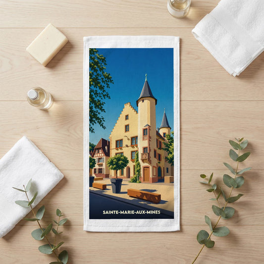 Serviette de bain souvenir de la ville de Sainte-Marie-aux-Mines avec une illustration stylisée d'un bâtiment historique alsacien.