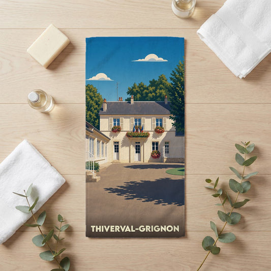 Serviette de bain souvenir de Thiverval-Grignon avec une illustration stylisée d'un bâtiment fleuri sous un ciel bleu.