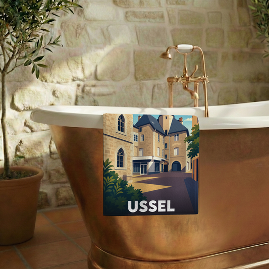 Serviette de bain souvenir de la ville d'Ussel avec une illustration stylisée de ses bâtiments historiques.