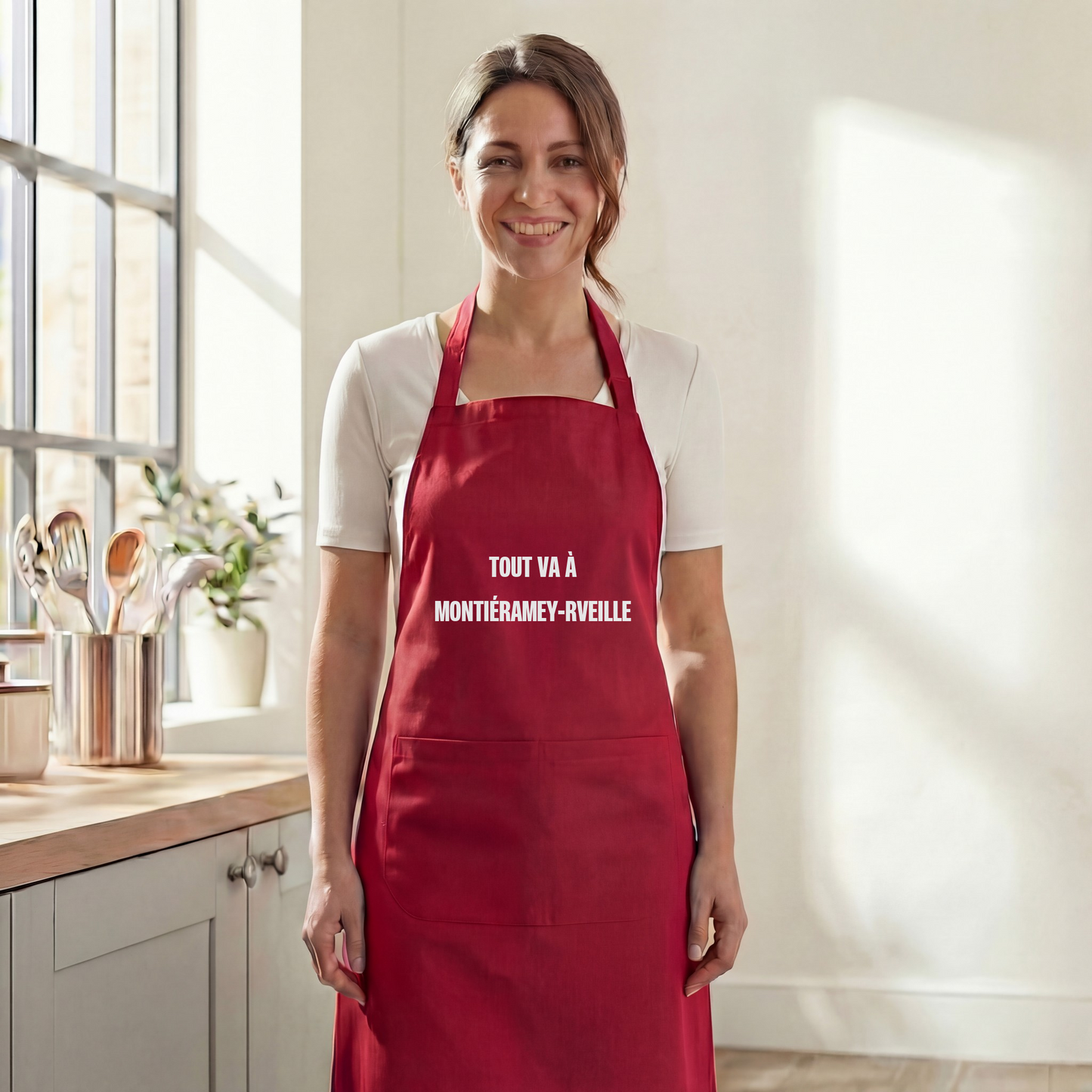 Tablier de cuisine rouge souvenir de la ville de Montiéramey avec l'inscription humoristique "Tout va à Montiéramey-rveille".
