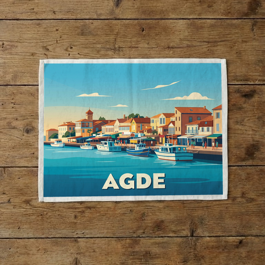 Torchon souvenir de la ville d'Agde avec une illustration stylisée de son port et de ses bateaux.