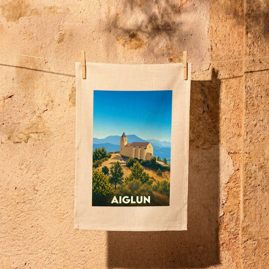 Torchon souvenir de la ville d'Aiglun avec une illustration stylisée d'une église perchée dans un paysage montagneux.