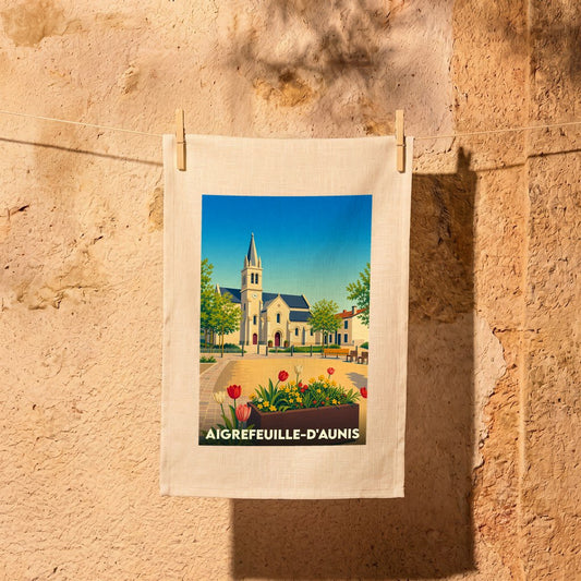Torchon souvenir de la ville d'Aigrefeuille-d'Aunis avec une illustration stylisée de son église et d'un parterre de fleurs.