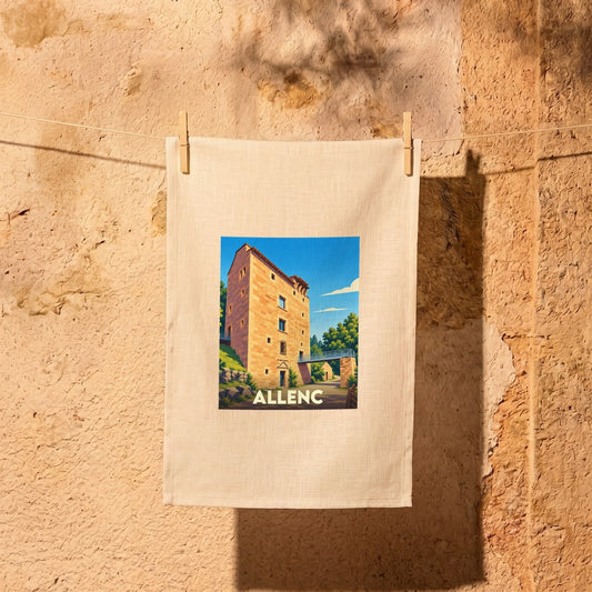 Torchon souvenir de la ville d'Allenc illustré d'un château médiéval stylisé, suspendu contre un mur en pierre.