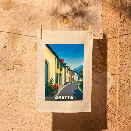 Torchon souvenir de la ville d'Arette illustrant une rue pittoresque aux façades colorées sous un ciel bleu.
