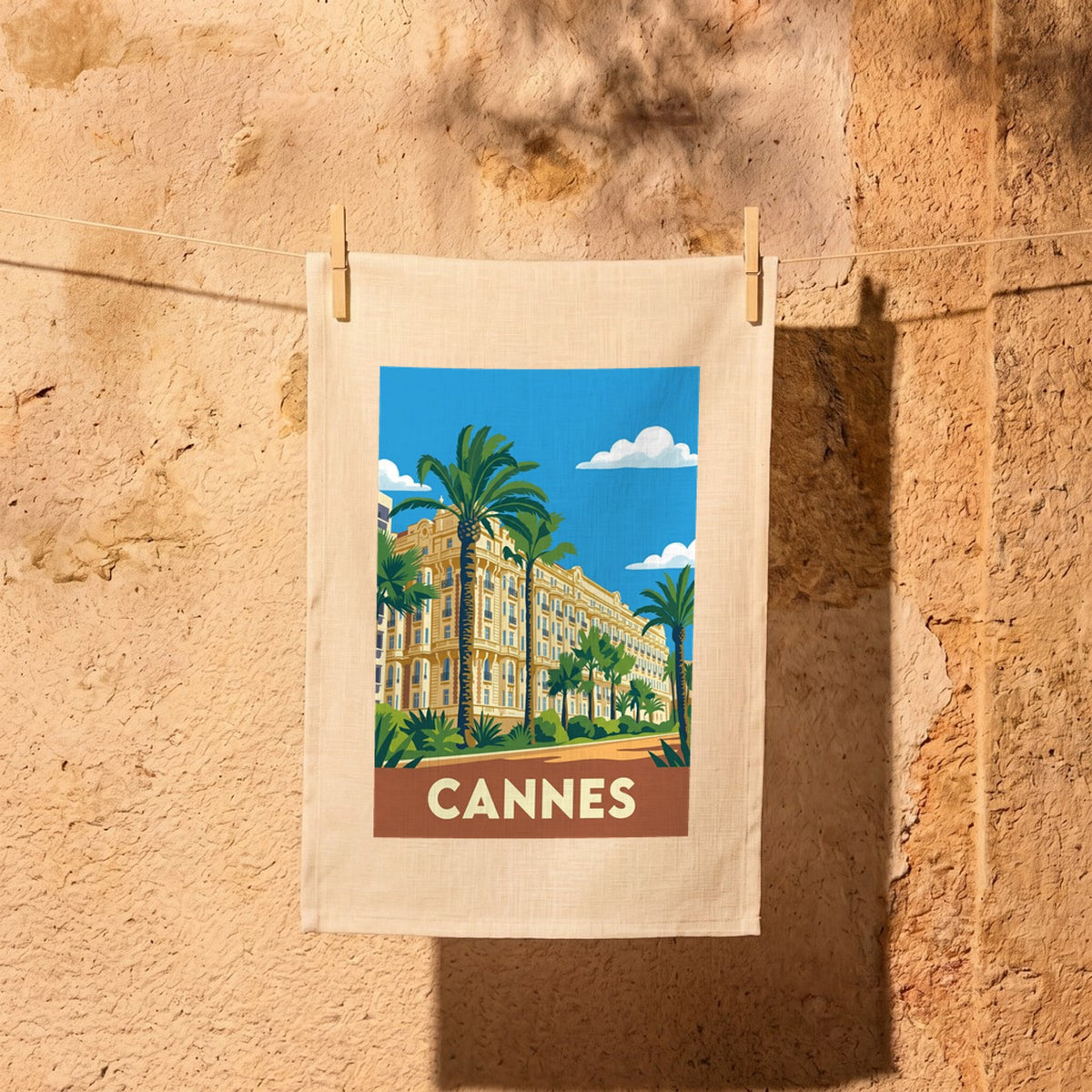 Torchon souvenir de la ville de Cannes avec une illustration stylisée représentant un palace et des palmiers.
