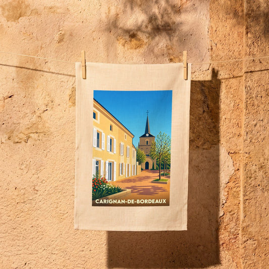 Torchon souvenir de Carignan-de-Bordeaux illustré d'une scène de village ensoleillée.