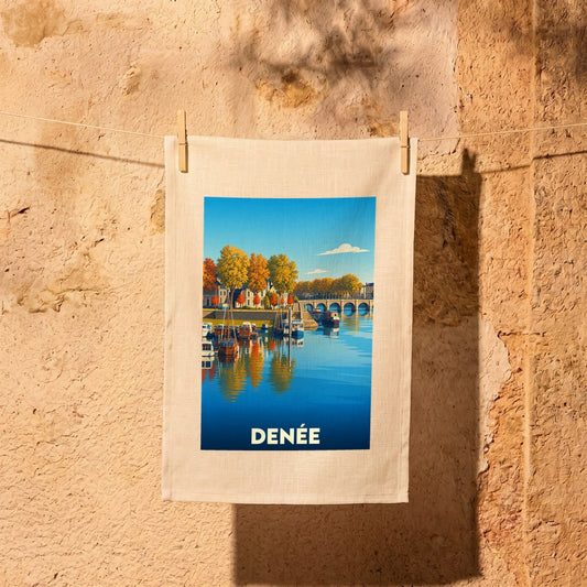 Torchon souvenir de la ville de Denée avec une illustration stylisée représentant un quai et ses bateaux en automne.