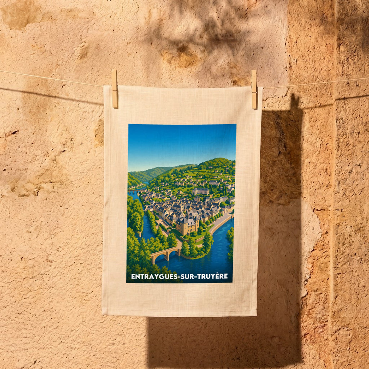 Torchon souvenir de la ville d’Entraygues-sur-Truyère avec une illustration stylisée et colorée du village bordé par l'eau.