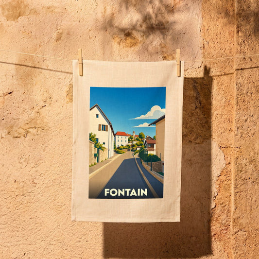 Torchon souvenir de la ville de Fontain avec une illustration stylisée d'une rue ensoleillée.
