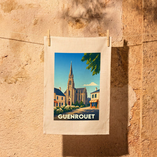 Torchon souvenir de la ville de Guenrouet illustré d'une vue stylisée de son église et suspendu devant un mur en pierre.