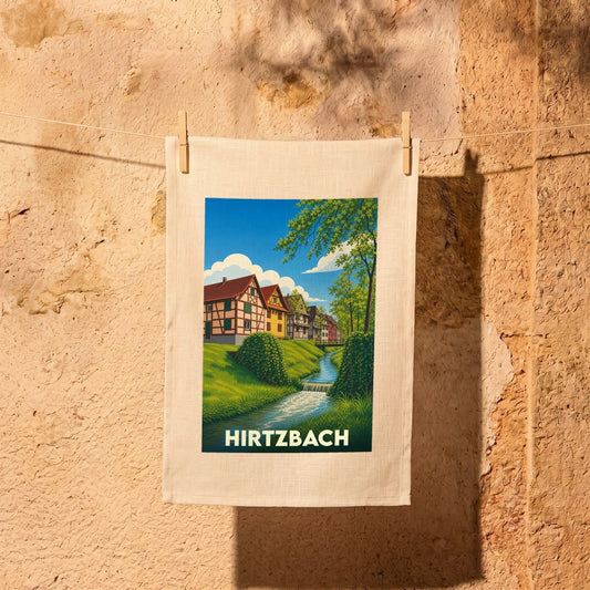 Torchon souvenir de la ville de Hirtzbach illustré d'un paysage pittoresque avec des maisons à colombages au bord de l'eau.