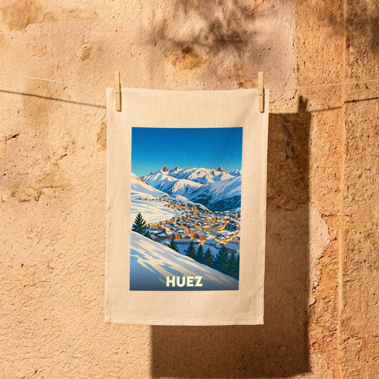 Torchon souvenir de la ville de Huez avec une illustration stylisée d'un village de montagne enneigé.
