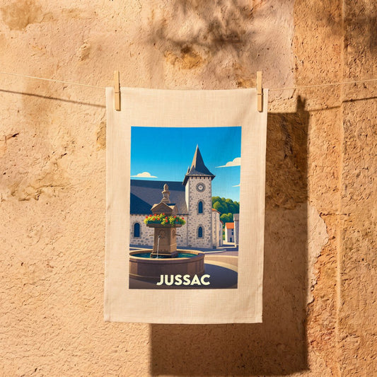Torchon souvenir de la ville de Jussac illustré d'une scène de village stylisée avec une fontaine et son église.