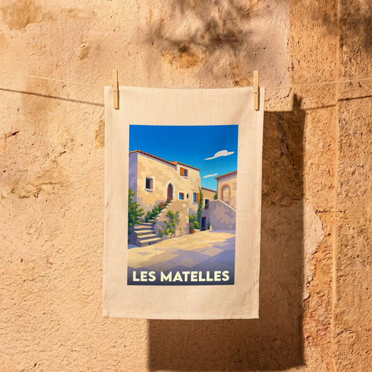 Torchon de cuisine souvenir de la ville de Les Matelles avec une illustration stylisée d'un village occitan.