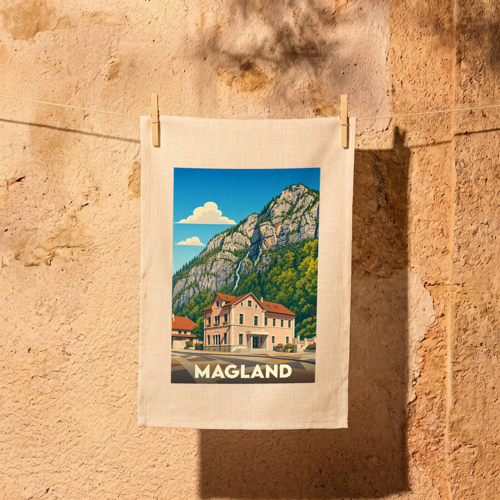 Torchon souvenir de la ville de Magland avec une illustration de style affiche vintage représentant une maison devant une montagne.