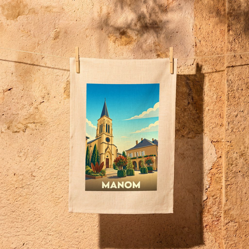 Torchon souvenir de la ville de Manom avec une illustration stylisée de son église sous un ciel bleu.