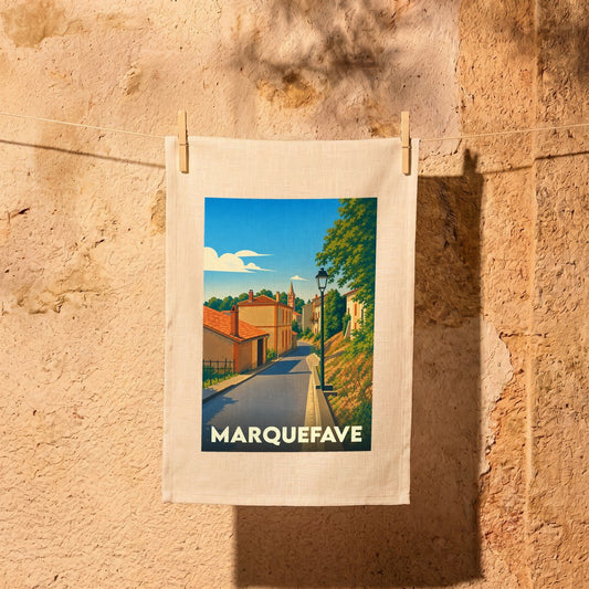 Torchon souvenir de la ville de Marquefave orné d'une illustration stylisée d'une rue ensoleillée.