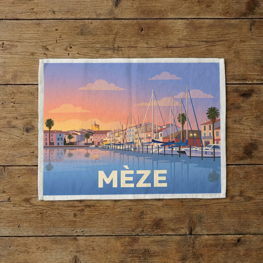 Torchon souvenir de la ville de Mèze avec une illustration stylisée du port au coucher du soleil.