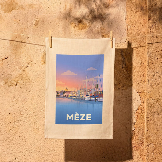 Torchon souvenir de la ville de Mèze avec une illustration stylisée du port au coucher du soleil.