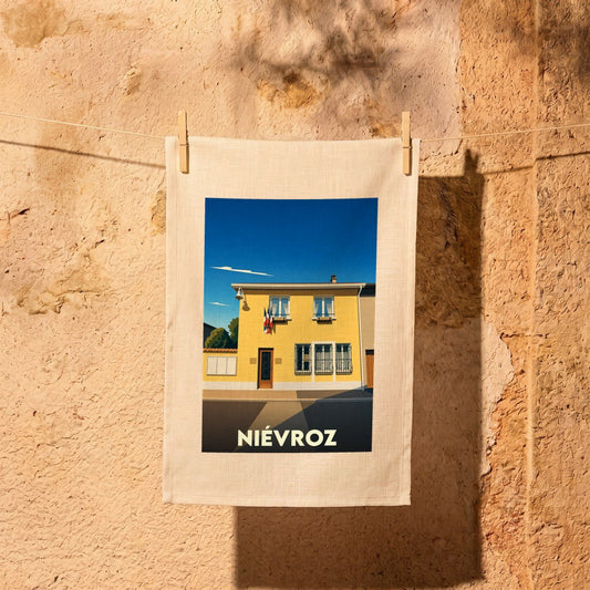 Torchon souvenir de la ville de Niévroz avec une illustration stylisée d'un bâtiment jaune.