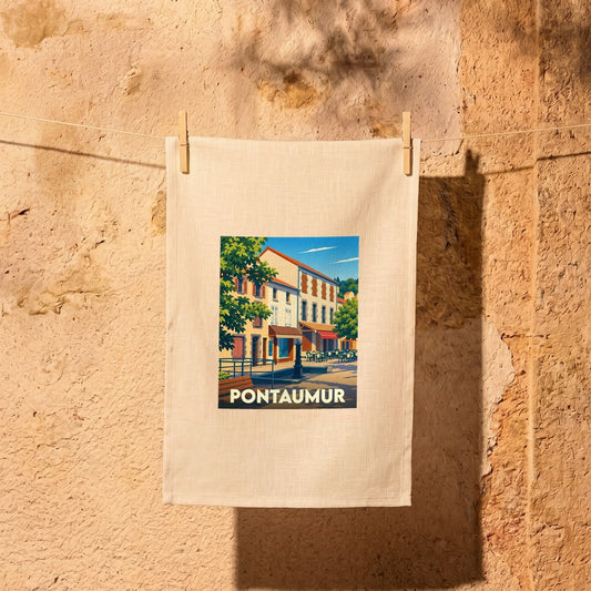 Torchon souvenir de la ville de Pontaumur avec une illustration colorée suspendu sur un fil à linge devant un mur en pierre.