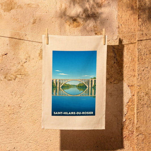 Torchon souvenir de Saint-Hilaire-du-Rosier illustré d'un pont se reflétant dans l'eau sous un ciel bleu.